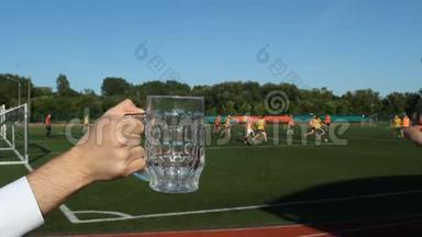 在足球场的背景下，一个男人在杯子里倒啤酒